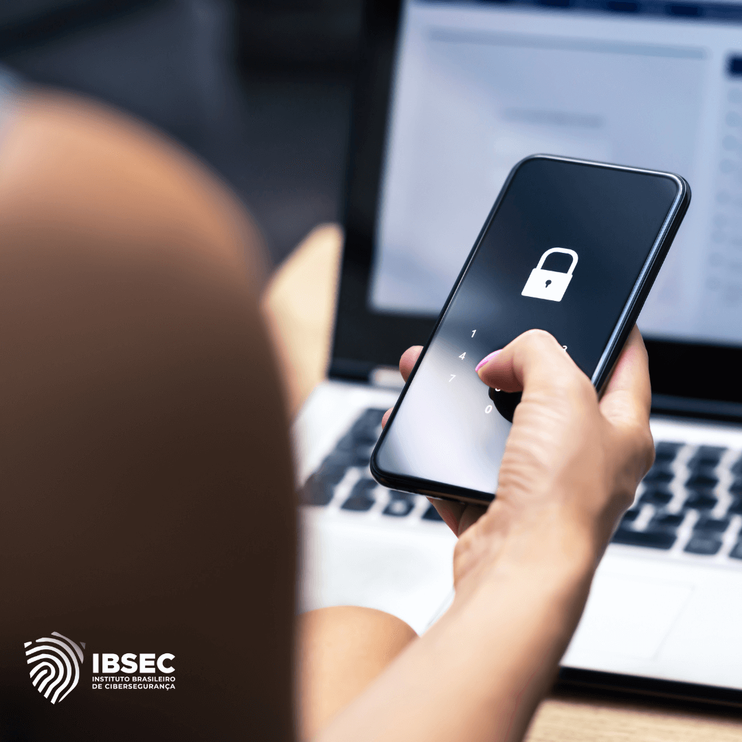 Pessoa segurando um smartphone, desbloqueando a tela que exibe um ícone de cadeado. Ao fundo, um laptop desfocado. No canto inferior esquerdo, o logotipo do Instituto Brasileiro de Cibersegurança (IBSEC).