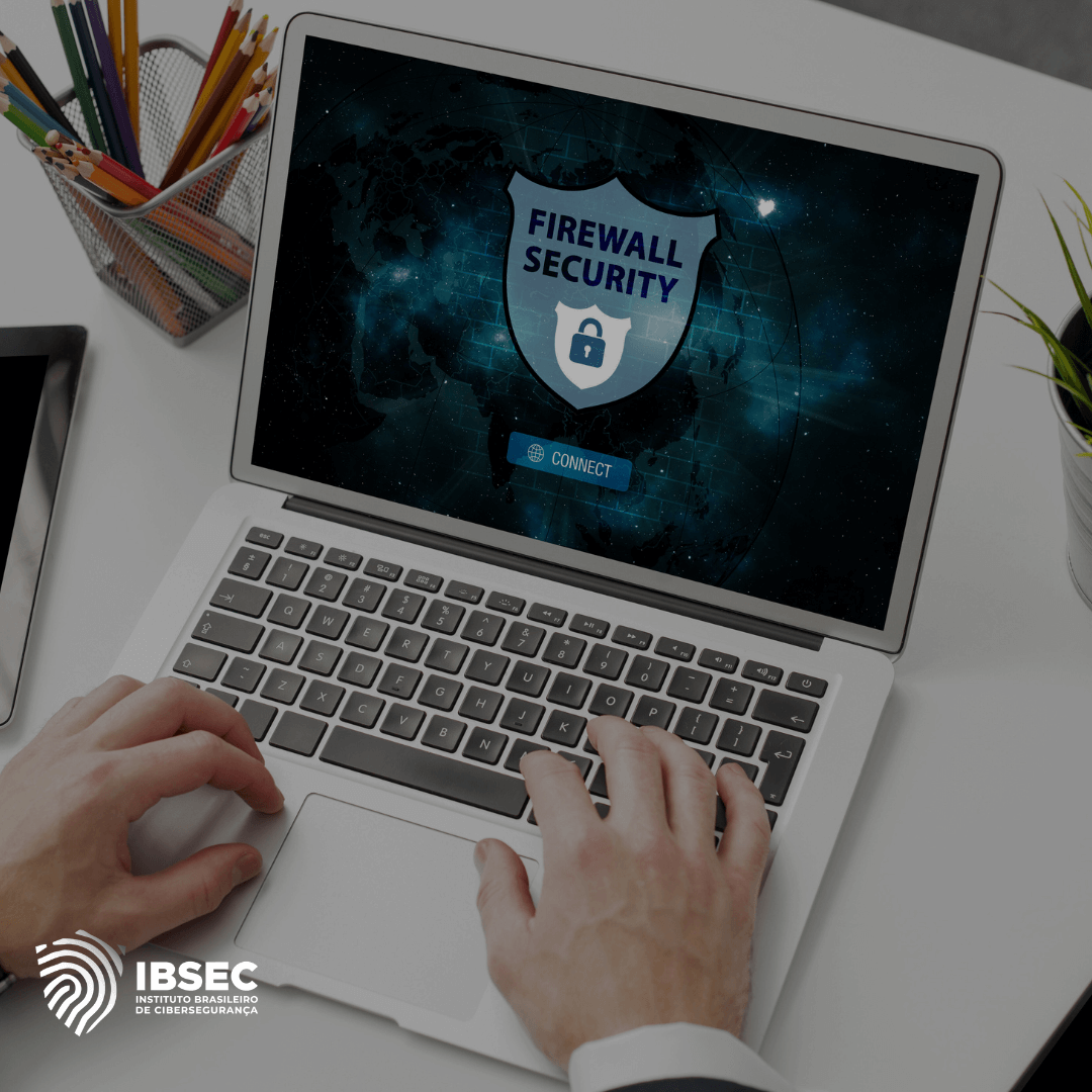 Mãos digitando em um notebook aberto sobre uma mesa, e um pote com lápis ao lado dele. Na tela do notebook um escudo com o escrito: firewall security e um escudo embaixo