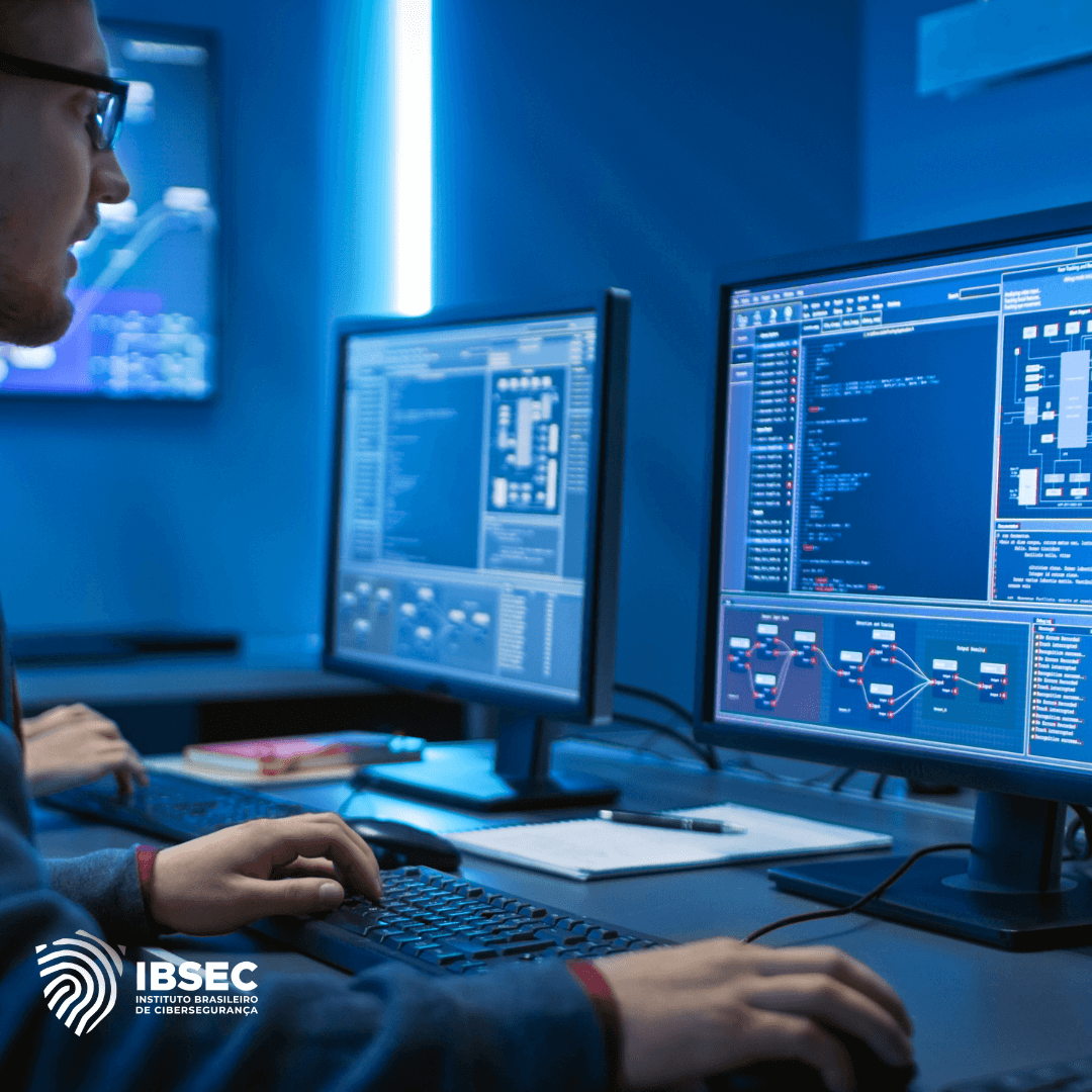 A imagem mostra uma pessoa usando óculos, sentada em frente a dois monitores de computador em um ambiente de trabalho. Os monitores exibem códigos de programação e diagramas de fluxo. No canto inferior esquerdo da imagem, está o logotipo do IBSEC (Instituto Brasileiro de Cibersegurança). O ambiente tem iluminação azulada, sugerindo um centro de operações de segurança cibernética.