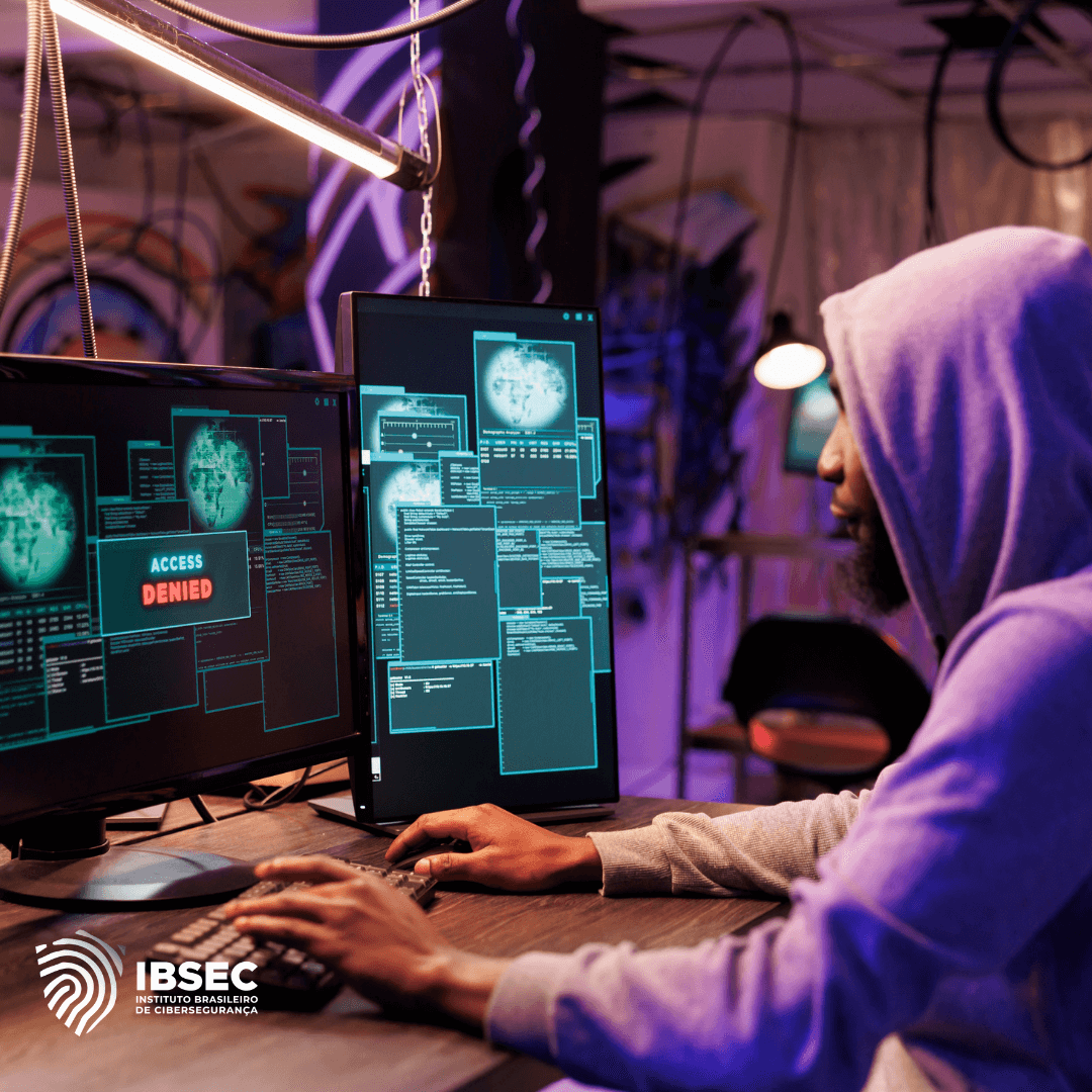 Um profissional de cibersegurança, usando um moletom com capuz, trabalha em frente a dois monitores de computador. Os monitores exibem várias janelas com códigos e gráficos, incluindo uma mensagem de 'ACCESS DENIED'. A imagem inclui o logotipo do Instituto Brasileiro de Cibersegurança (IBSEC) no canto inferior esquerdo.