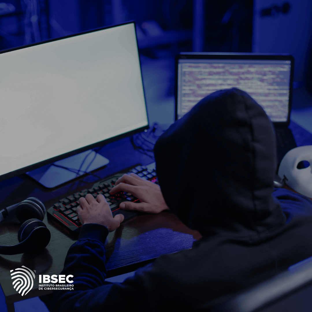 A imagem mostra uma pessoa com um capuz preto sentada em frente a dois monitores de computador. Um dos monitores está com a tela em branco, enquanto o outro exibe linhas de código. Há um par de fones de ouvido ao lado do teclado e um teclado retroiluminado. No canto inferior esquerdo, está o logotipo do IBSEC - Instituto Brasileiro de Cibersegurança. A cena é iluminada com uma luz azulada, sugerindo um ambiente de cibersegurança ou hacking.