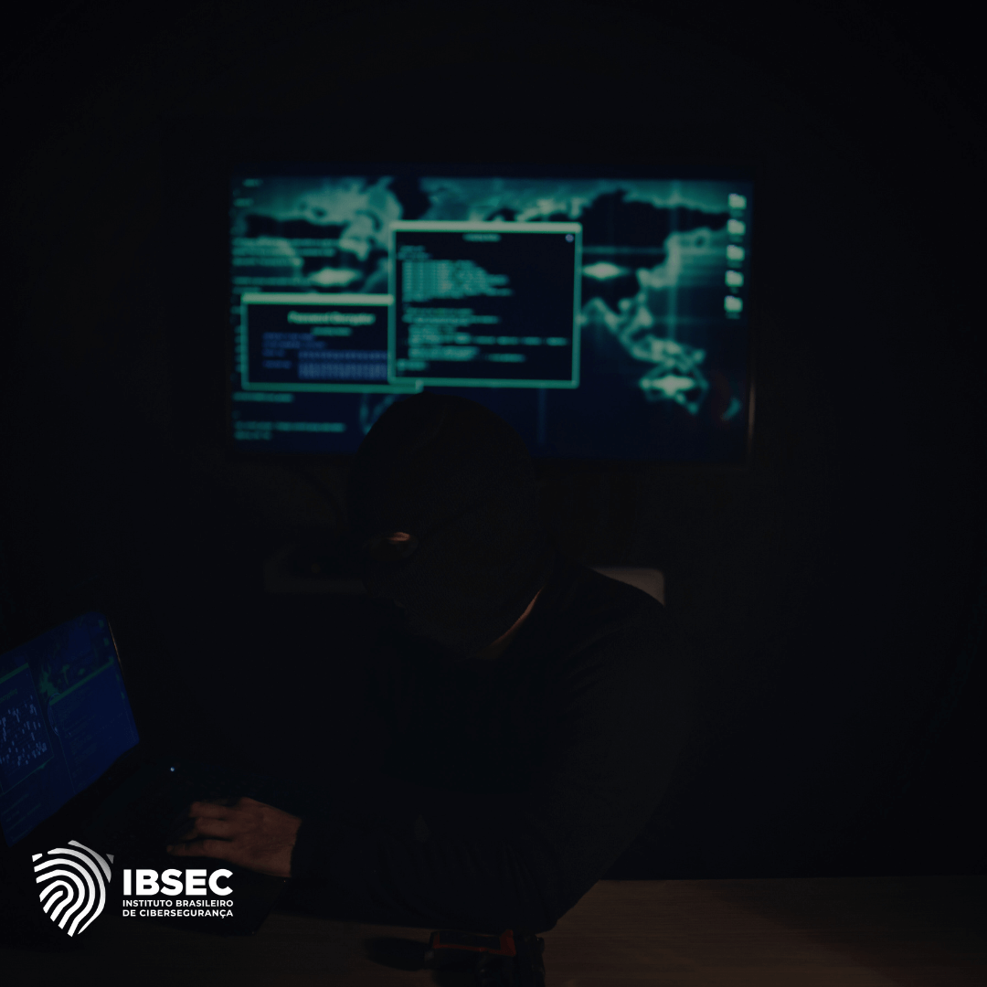 Imagem de uma pessoa usando uma máscara preta, operando um laptop em um ambiente escuro. Ao fundo, uma tela grande exibe códigos e gráficos de segurança cibernética. No canto inferior esquerdo, o logotipo do IBSEC (Instituto Brasileiro de Cibersegurança) é visível. A cena sugere uma atividade relacionada à segurança digital, possivelmente simulando um ataque cibernético.