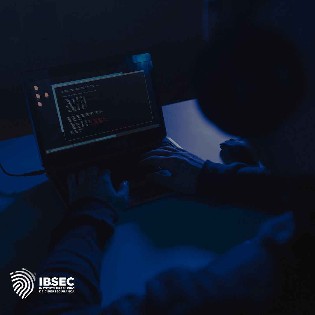 Pessoa usando um laptop em um ambiente escuro, com a tela exibindo códigos de programação. A imagem sugere atividades relacionadas à cibersegurança. No canto inferior esquerdo, há o logotipo do IBSEC (Instituto Brasileiro de Cibersegurança)