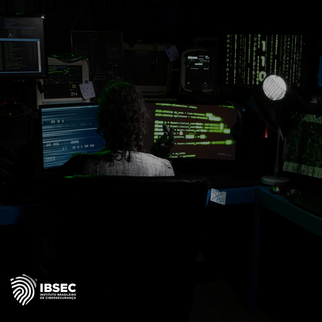 Profissional de cibersegurança sentado em frente a múltiplos monitores em um ambiente escuro, analisando códigos e dados em telas com interface de programação. O logo do IBSEC (Instituto Brasileiro de Cibersegurança) aparece no canto inferior esquerdo da imagem.