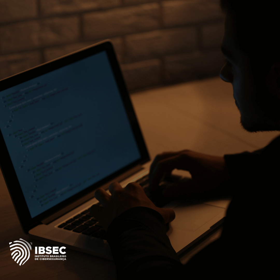 Homem utilizando um laptop em ambiente com baixa iluminação, escrevendo ou revisando código em uma tela com fundo escuro. No canto inferior esquerdo, há o logotipo do IBSEC (Instituto Brasileiro de Cibersegurança).