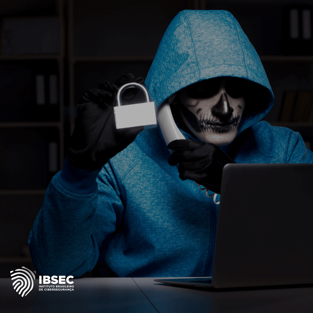 Imagem de um hacker com capuz azul e máscara de caveira segurando um cadeado branco e falando ao telefone. Ele está sentado em frente a um laptop, em um ambiente escuro e de aparência ameaçadora. O logo do Instituto Brasileiro de Cibersegurança (IBSEC) está posicionado no canto inferior esquerdo da imagem, reforçando o tema de segurança digital.