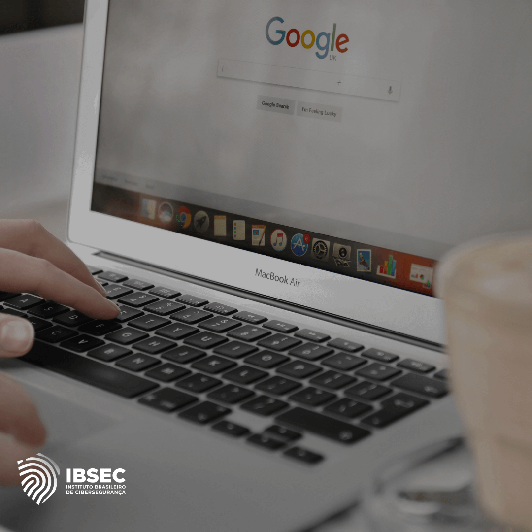 Imagem de uma pessoa digitando em um laptop MacBook Air com a página inicial do Google aberta no navegador. Ao lado do computador, há um copo de café desfocado. No canto inferior esquerdo, está o logotipo do IBSEC (Instituto Brasileiro de Cibersegurança). A cena sugere uma atividade de busca ou navegação online.