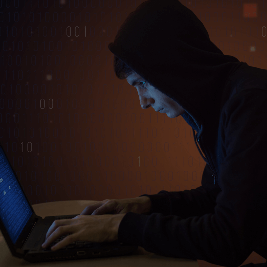 Homem usando capuz sentado em frente a um laptop, concentrado na tela enquanto digita. O fundo exibe números binários em tom escuro, criando um ambiente digital. A imagem evoca o conceito de cibersegurança, testes de invasão ou hacking ético.