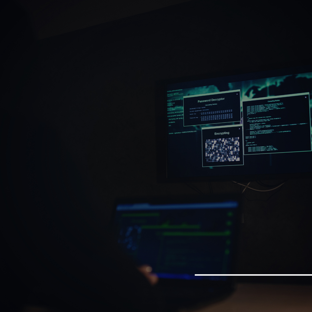 A imagem mostra uma cena escura de um ambiente de cibersegurança, com um computador portátil em primeiro plano e uma tela maior ao fundo. Na tela maior, há diversas janelas de software de segurança exibindo processos como descriptografia de senhas e criptografia de dados. O clima é de alta tecnologia, sugerindo a análise ou execução de atividades relacionadas à segurança da informação.