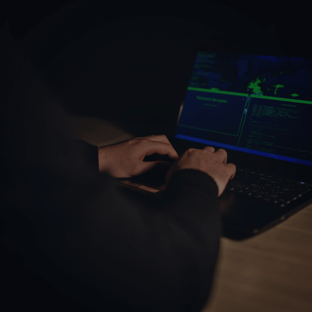 Pessoa usando laptop em ambiente escuro, com tela exibindo códigos e gráficos, sugerindo atividades relacionadas a segurança cibernética ou monitoramento da dark web.