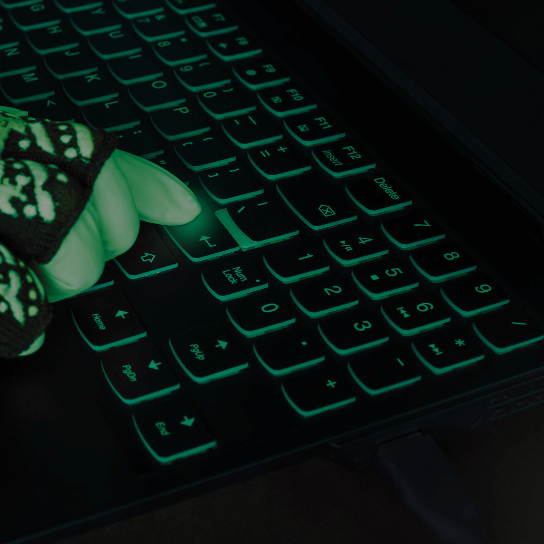 Mão com luva de esqueleto digitando em um teclado iluminado, destacando as teclas com uma luz verde neon, dando uma aparência sombria e tecnológica.